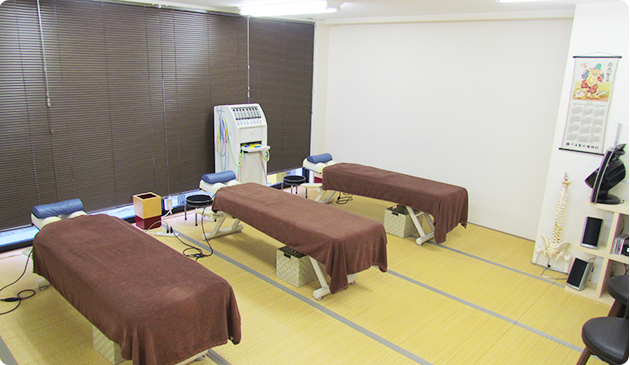 明るい色の畳の上に治療用ベッドが３台、奥に中周波治療器が置いてある院内の写真